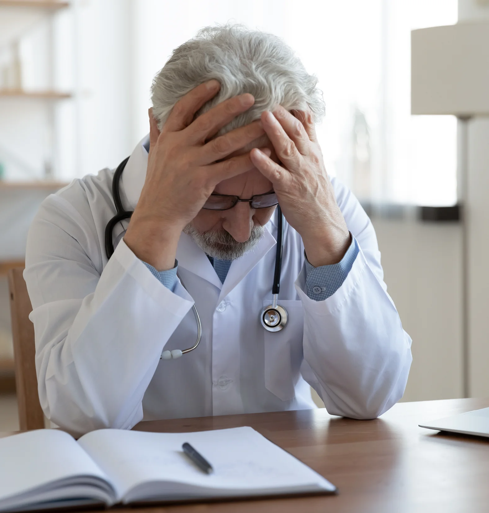 Tired doctor holding his head in frustration at his desk.